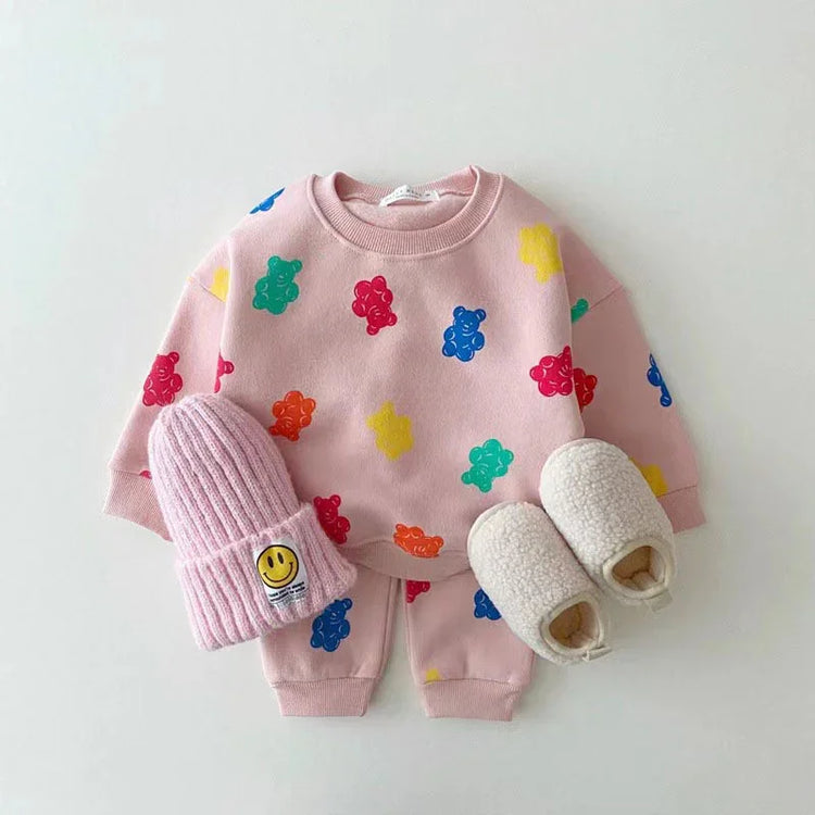 Pink toddler outfit with colorful bear print sweatshirt, matching joggers, knit beanie, and fuzzy slippers