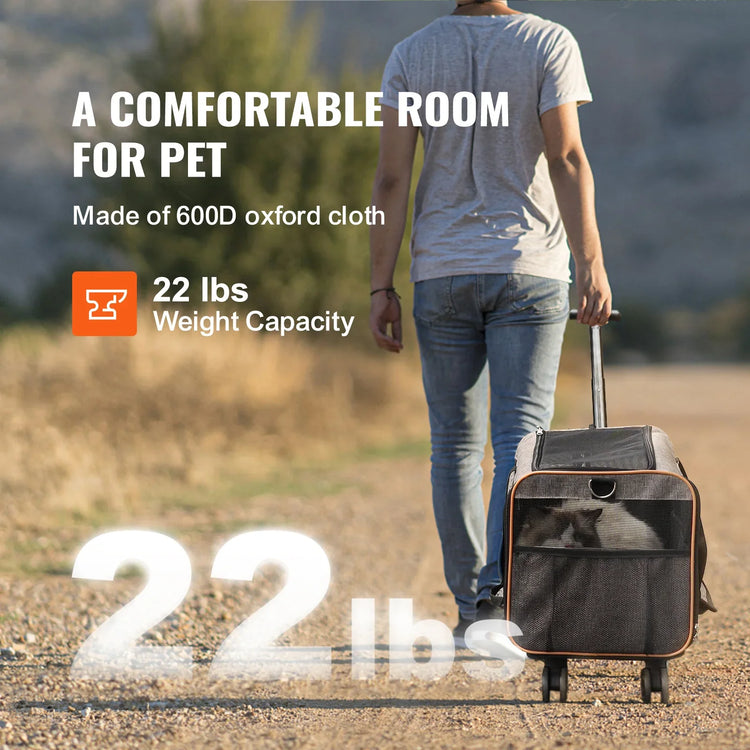 Man wearing light grey t-shirt and blue jeans, walking outdoors pulling a black oxford cloth pet carrier with wheels.