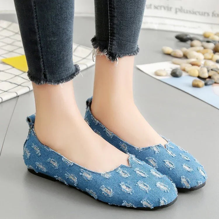Light blue distressed denim slip-on flats with raw edges, paired with black skinny jeans