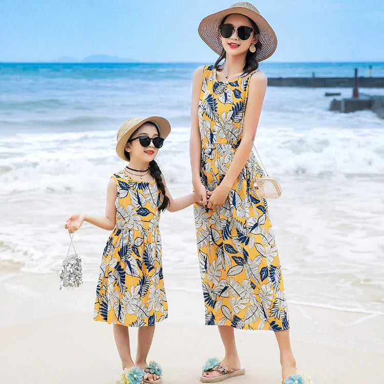 Woman and girl in matching sleeveless yellow floral print summer dresses on the beach