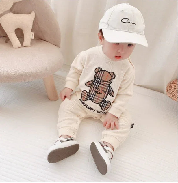 Baby in cream ribbed bear-print jumpsuit, white cap, and sneakers, casual loose fit