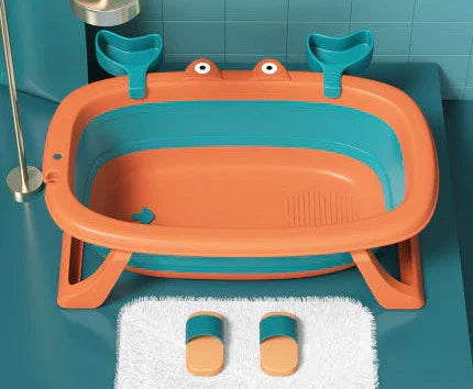 Orange and teal collapsible baby bathtub with built-in seat and matching slippers on a white mat