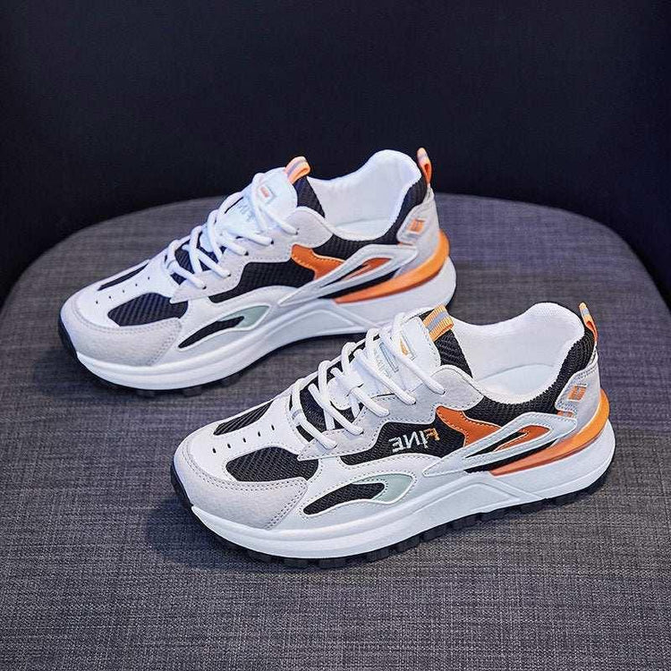 White, black, and orange chunky sneakers with mesh and suede panels on a grey chair.
