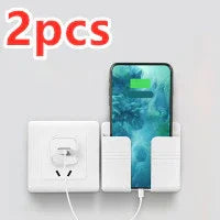Wall-mounted white plastic phone holder with charging slot, shown with smartphone and outlet
