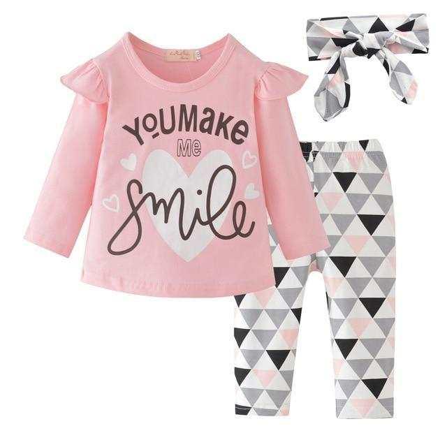 Pink long-sleeve ruffle top with printed text, geometric leggings, and matching headband for kids