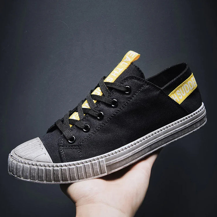 Black canvas sneaker with yellow accents, low-top design, and a gray rubber sole