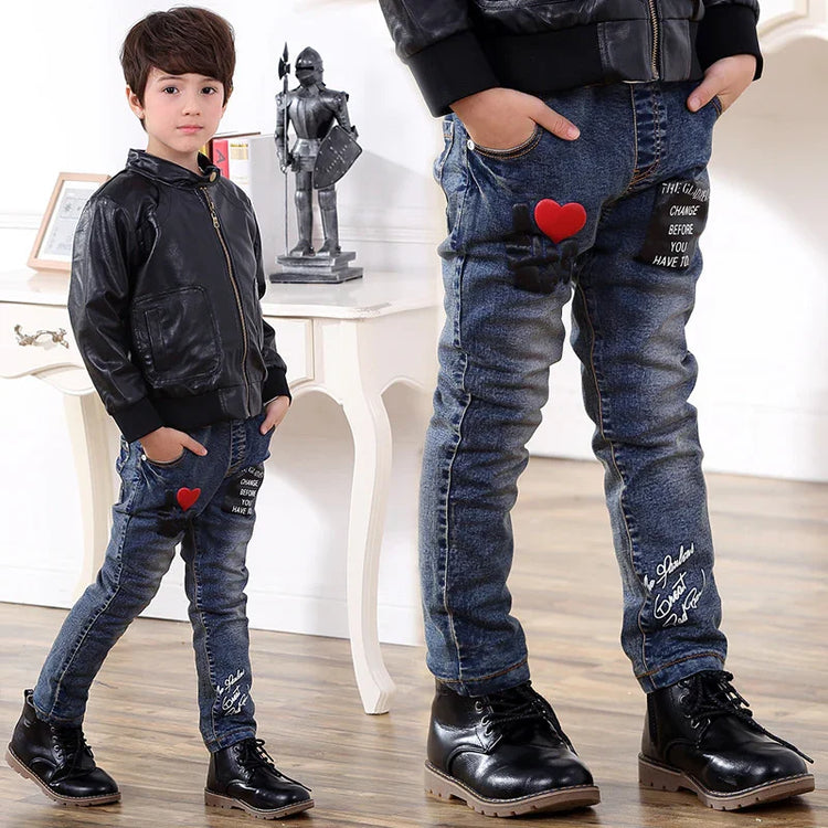 Boy in black faux leather jacket and slim fit blue jeans with red heart patch and boots