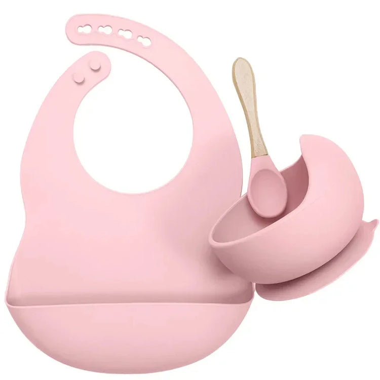 Pink silicone bib, suction bowl, and spoon set for babies or toddlers, modern design.