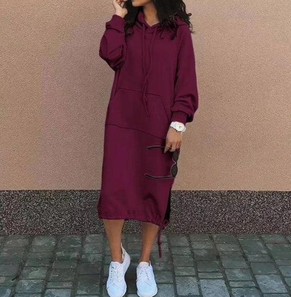 Woman wearing a loose-fitting burgundy hoodie dress with long sleeves and drawstring hem, styled with white sneakers.