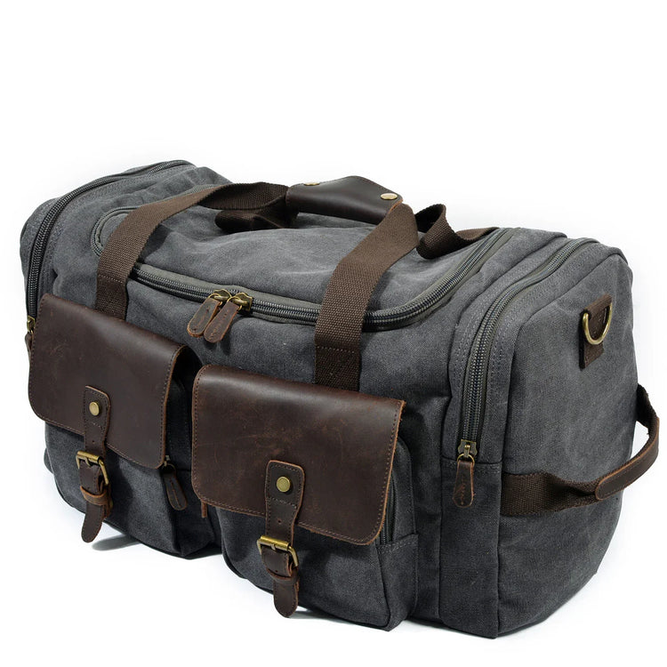 Grey canvas duffel bag with brown leather pockets, rugged straps, and brass hardware