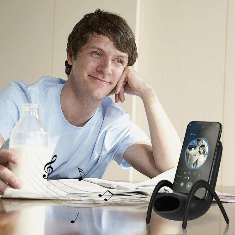 Man in light blue relaxed fit t-shirt at table, listening to music from smartphone on unique black cradle
