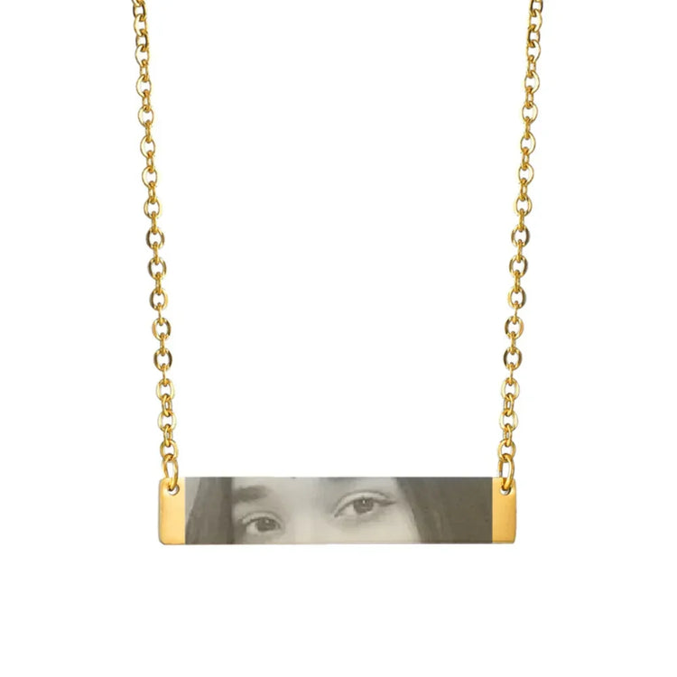 Gold chain necklace with horizontal bar pendant featuring engraved face details, minimalist style
