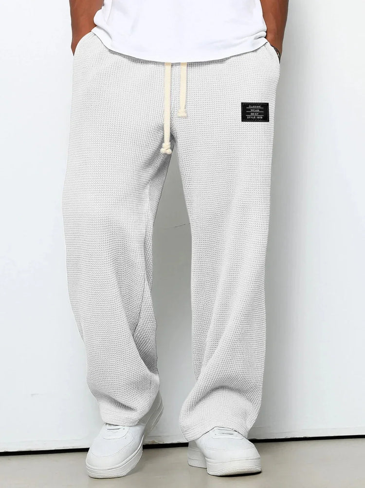 White waffle knit drawstring pants with relaxed fit and side patch, styled with white sneakers.