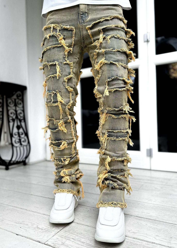 Distressed tan denim jeans with heavy frayed details and slim fit, worn with white sneakers