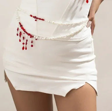 White bodycon mini skirt with pearl and red bead chain detail, fitted style, split hem