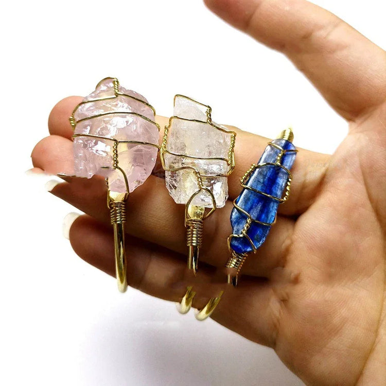 Hand holding wire-wrapped crystal rings in pink, clear, and blue, bold gemstone jewelry.