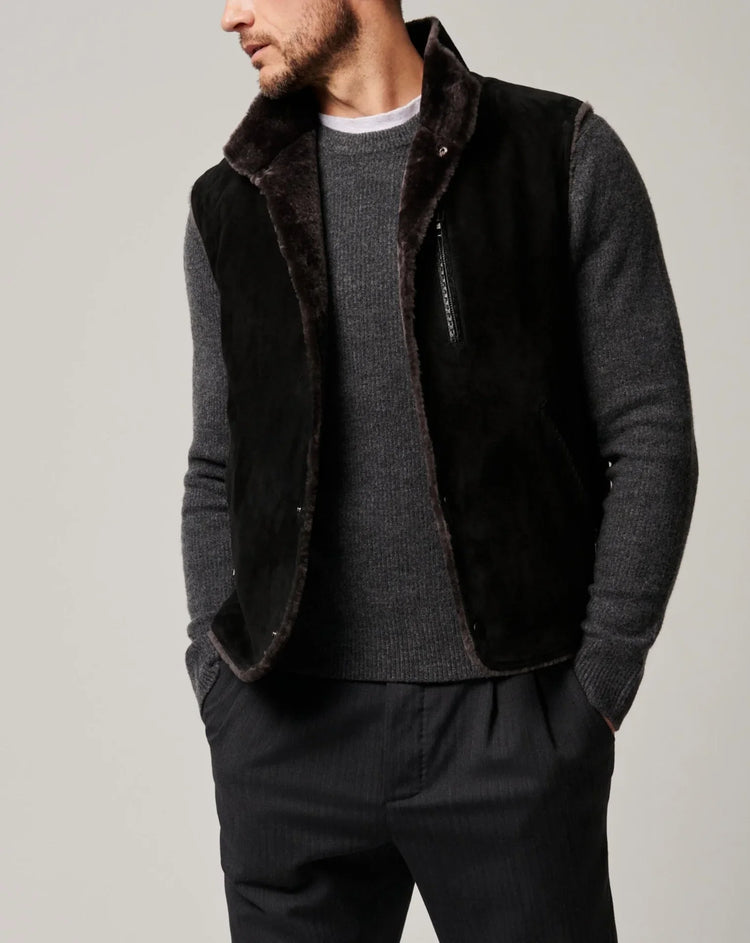 Man wearing black shearling vest over gray knit sweater and dark tailored pants, modern fit