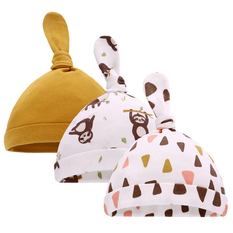 Set of three soft cotton baby hats, one solid mustard, two with playful animal and geometric prints, all featuring knotted tops.