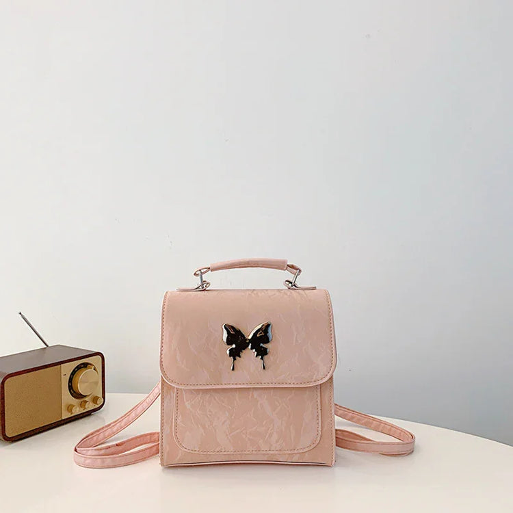 Pastel pink faux leather mini backpack with butterfly accent and adjustable straps, boxy fit
