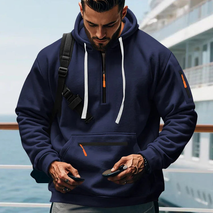 Man wearing a navy blue pullover hoodie with front zip pocket, orange accents, and relaxed fit