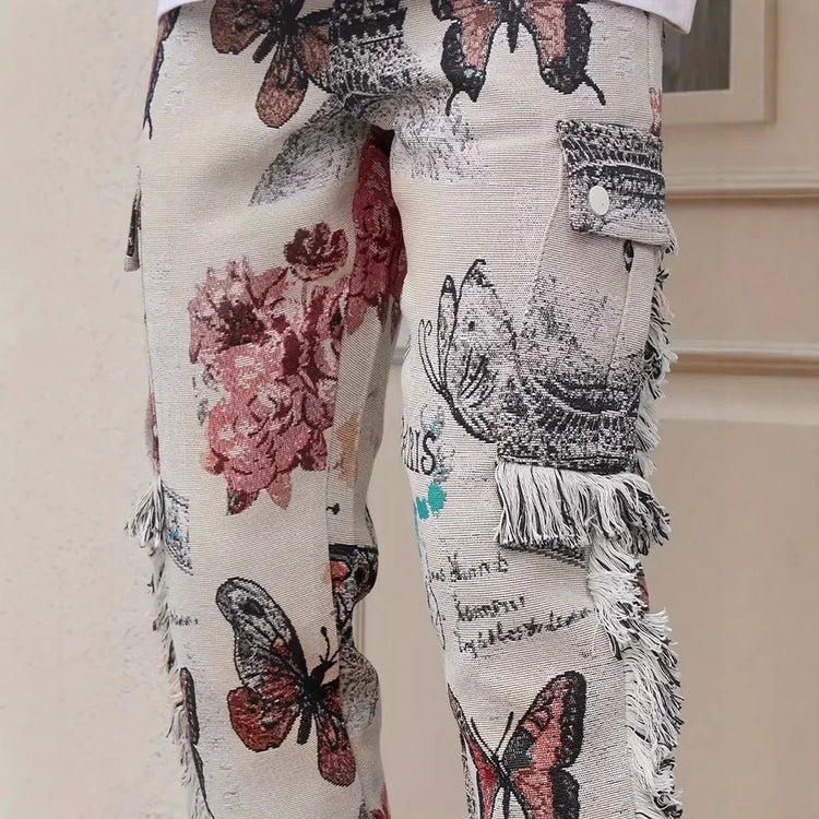 Beige streetwear pants with floral and butterfly print, fringe details, and relaxed fit