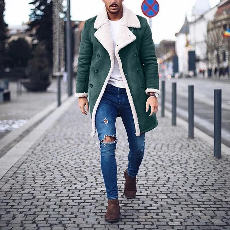 Man in a green shearling-lined long coat, ripped blue skinny jeans, and brown boots walking on a city street.