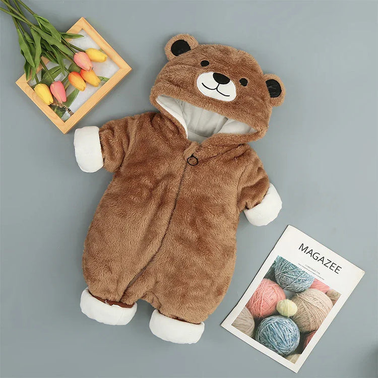 Brown plush bear onesie for babies with hood, white cuffs, and cozy fit, laid flat on gray background.