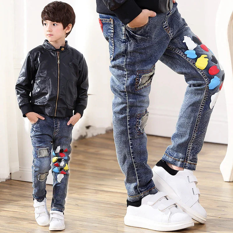 Boy wearing black faux leather jacket and slim fit blue jeans with colorful patches