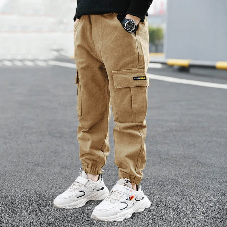 Beige cargo jogger pants with pockets, relaxed fit, paired with white chunky sneakers.