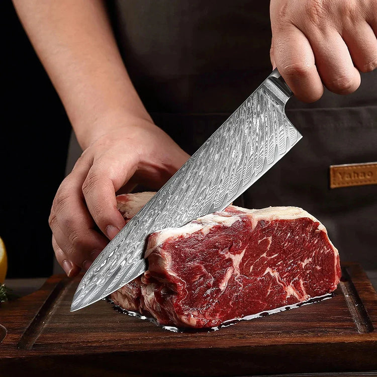 Hand slicing raw marbled beef with a patterned chef knife on a wooden cutting board