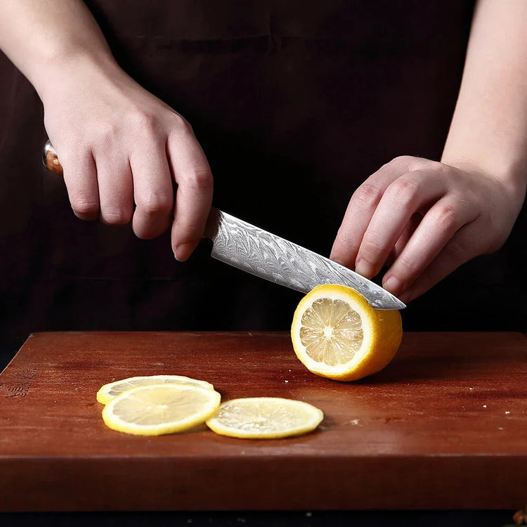 Person using a patterned steel kitchen knife to slice a lemon on a wooden cutting board