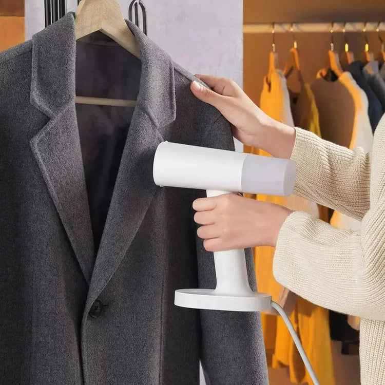 Steaming a gray wool coat with a handheld garment steamer in a closet setting