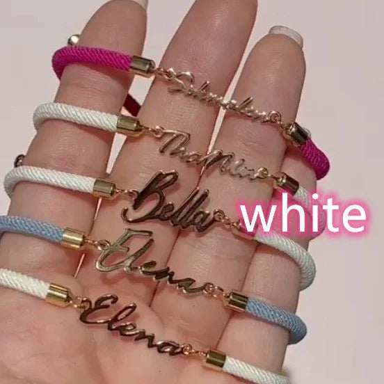 Personalized nameplate bracelets with gold script, white, pink, and blue woven cords, adjustable fit.