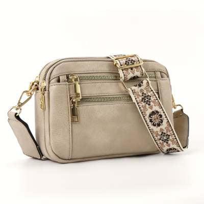 Beige faux leather crossbody bag with gold zippers and a wide floral adjustable strap.