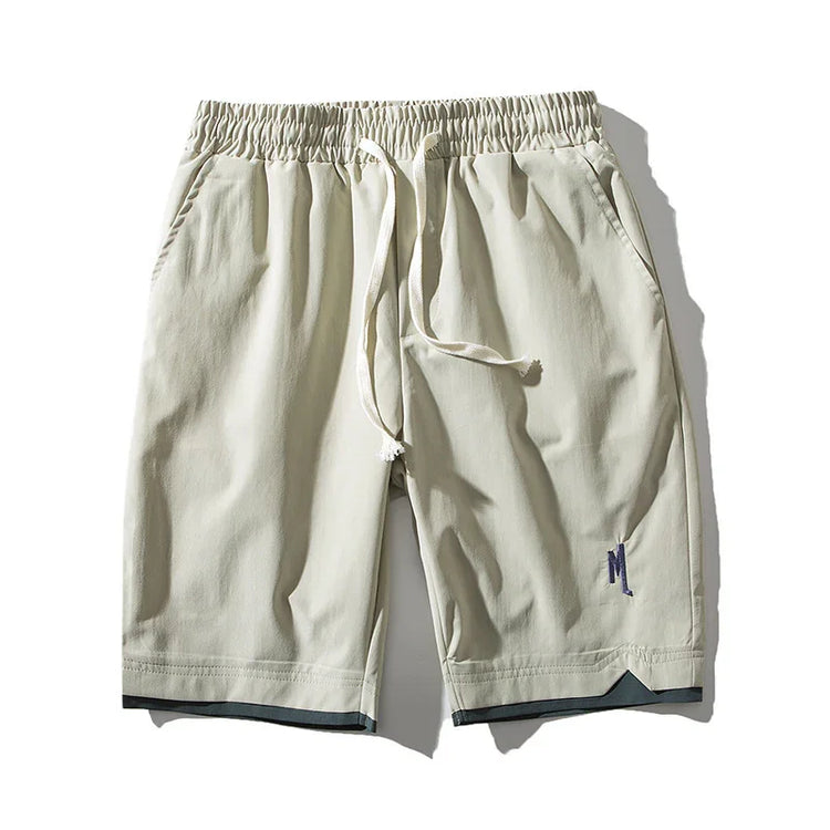 Beige relaxed-fit streetwear shorts with elastic waistband, drawstring, and subtle embroidery.