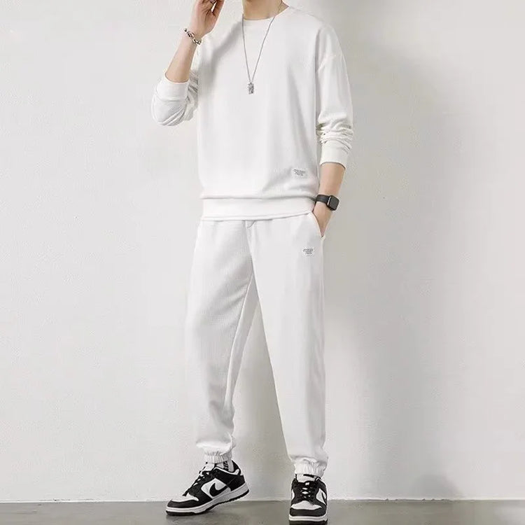 Man wearing a relaxed fit white sweatshirt and matching joggers, soft cotton material, minimalist streetwear style.