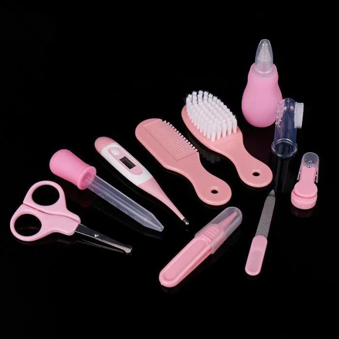 Pink baby grooming kit with brush, comb, scissors, thermometer, dropper, nail file on black background