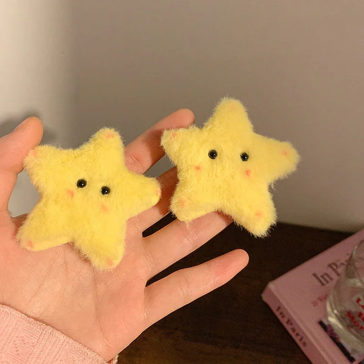 Hand holding two yellow plush star hair clips with cute embroidered faces, soft textured material.