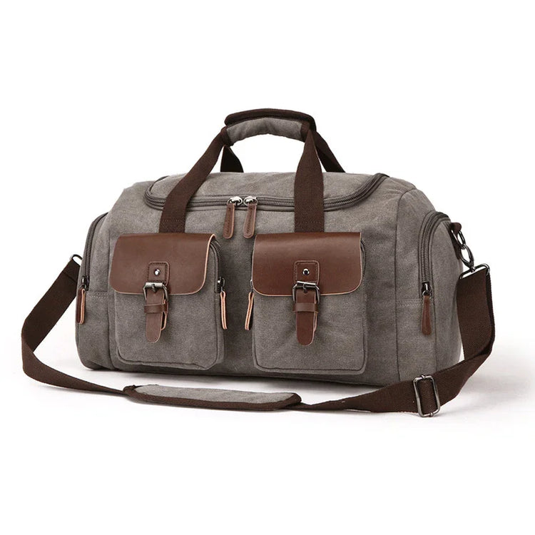 Gray canvas duffel bag with brown leather accents, buckle pockets, and adjustable strap