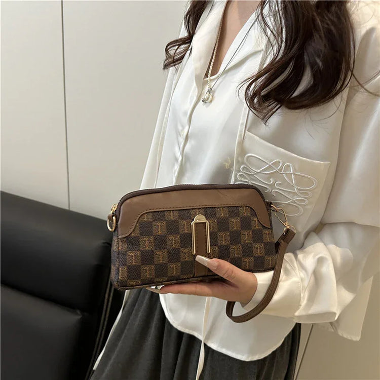 Woman wearing a loose white satin blouse with embroidered pocket, holding a brown plaid crossbody bag