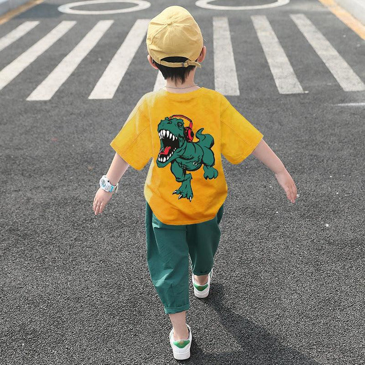 Kid in loose yellow dinosaur graphic t-shirt, green pants, and cap walking outdoors