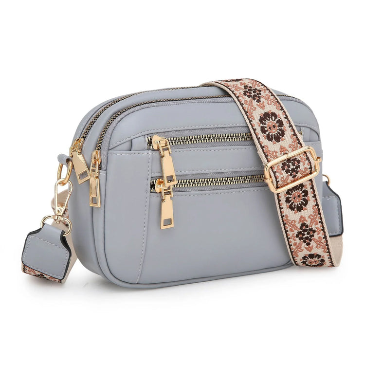 Light gray faux leather crossbody bag with gold zippers and a floral patterned strap