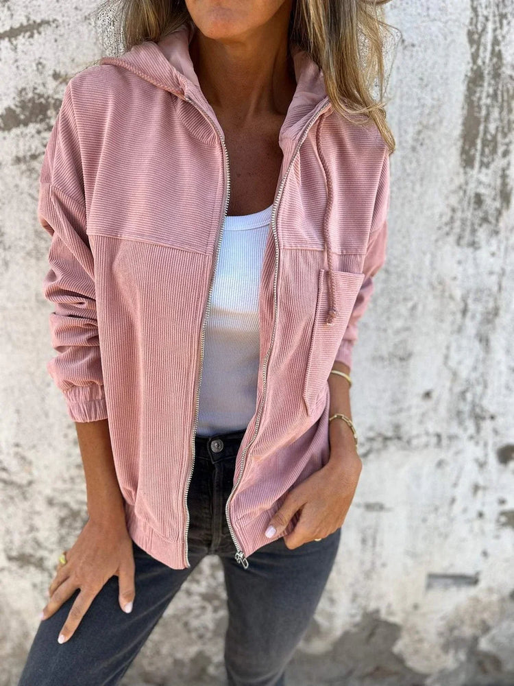 Woman wearing a pink corduroy zip-up jacket, white ribbed tank top, and black jeans