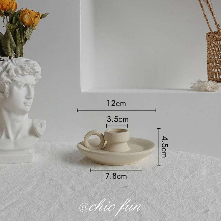 Minimalist beige ceramic candle holder with ring handle, placed on a white table, shown with dimensions 12cm wide, 4.5cm tall.