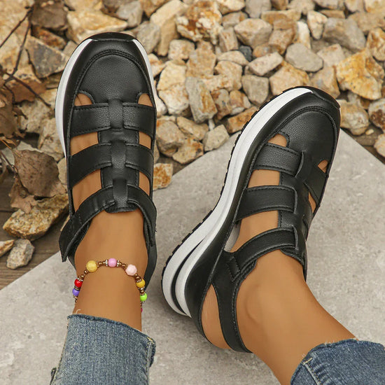Black leather strappy sandals with white soles, casual fit, worn with jeans on stone path