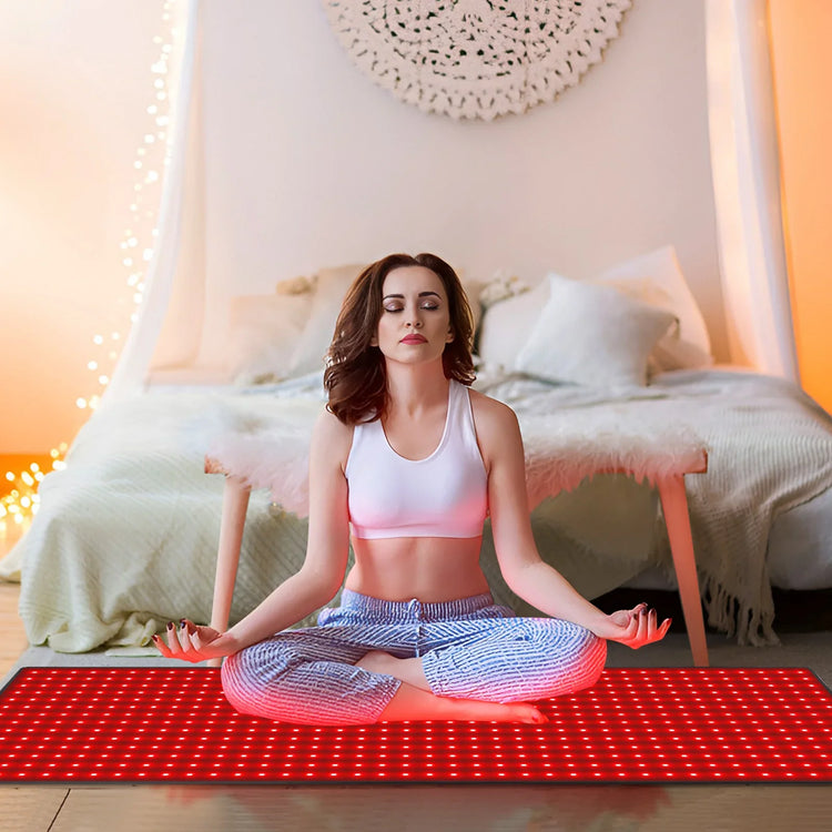 Woman in white cropped sports top and loose blue joggers meditating on red LED mat in bedroom