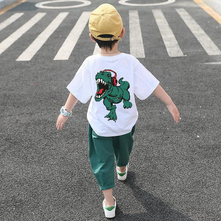 Child wearing loose white t-shirt with cartoon dinosaur graphic, green pants, yellow cap