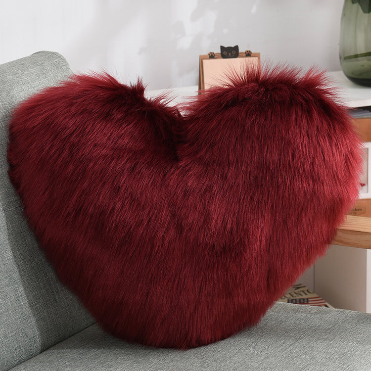 Plush heart-shaped burgundy faux fur pillow on a modern grey sofa