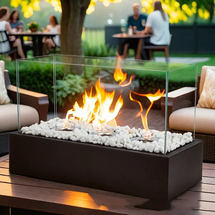 Modern glass tabletop fire pit with white stones on a patio, outdoor seating area in background