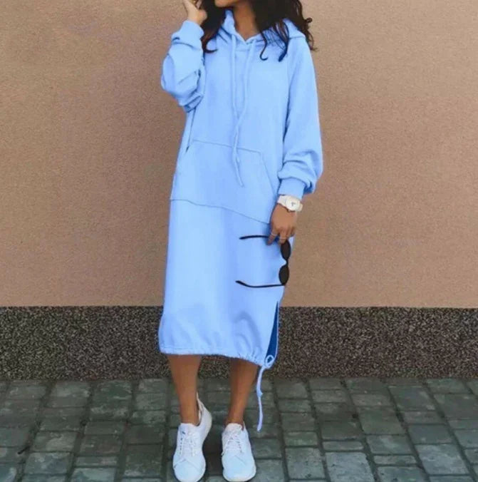 Woman wearing loose light blue hooded sweatshirt dress with drawstring hem and white sneakers